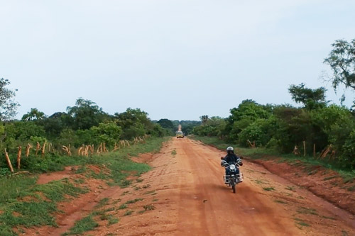 A Fellow rides a motorcycle down a rural dirt road