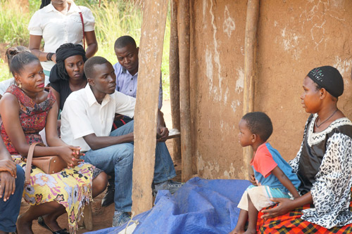 Fellows talk with a parent at her home as her child sits on her lap