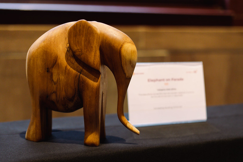 A wooden elephant sculpture sits on a silent auction table