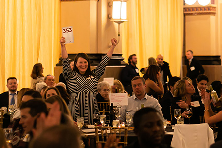 An ecstatic guest raises her hands and bidding paddle in triumph while bidding in the live auction