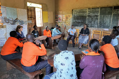 A group of Fellows, CEVs, and community leaders sit in a circle in discussion inside a classroom