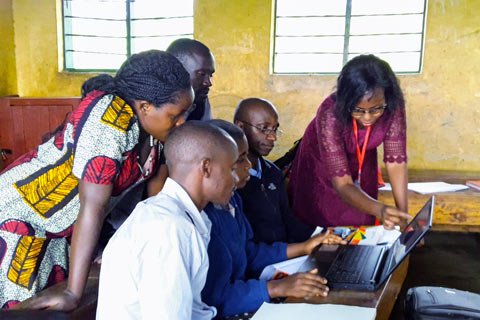 A Fellow teaches a group of community members how to use a laptop as they huddle around the screen