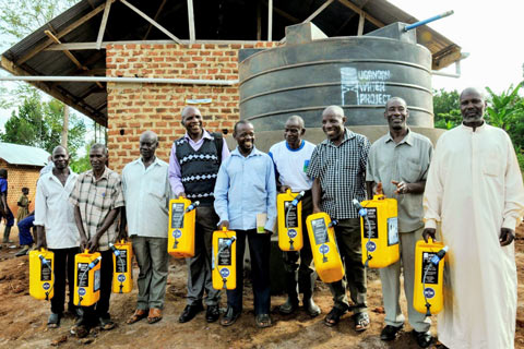 Community members hold specially designed yellow jerry cans in front of the water tank at their school