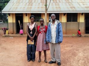 Building Tomorrow Fellow Catherine Nabalende (left) and Community Ambassador Mr. Wangoda (right) welcome Talindeka (middle) back to school.